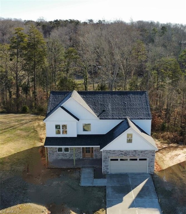 modern farmhouse style home with stone siding, driveway, and a view of trees