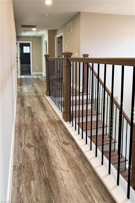 hallway featuring visible vents, attic access, baseboards, and wood finished floors