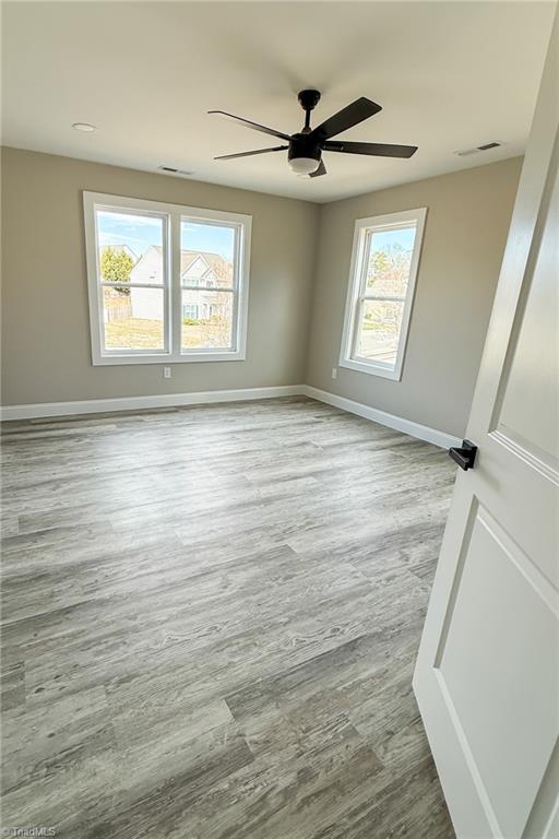 unfurnished room featuring wood finished floors, plenty of natural light, baseboards, and visible vents