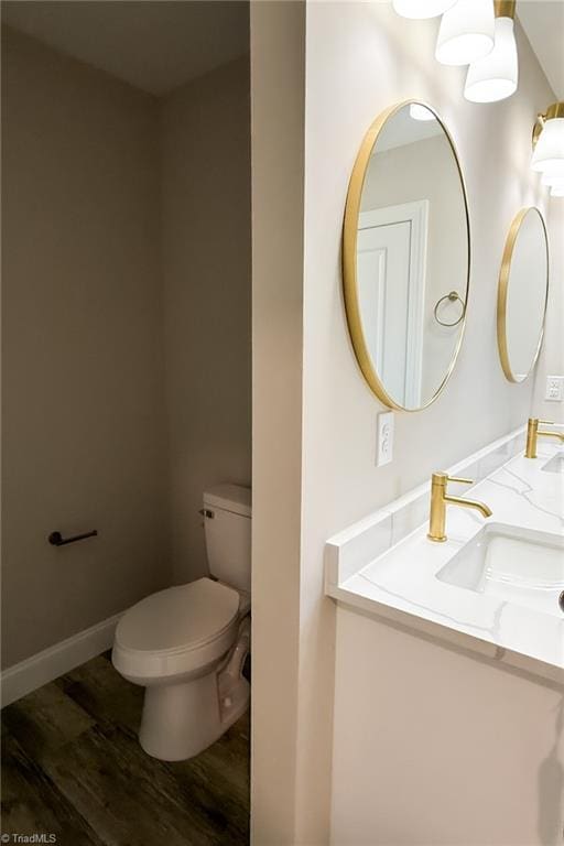 bathroom with vanity, toilet, wood finished floors, and baseboards