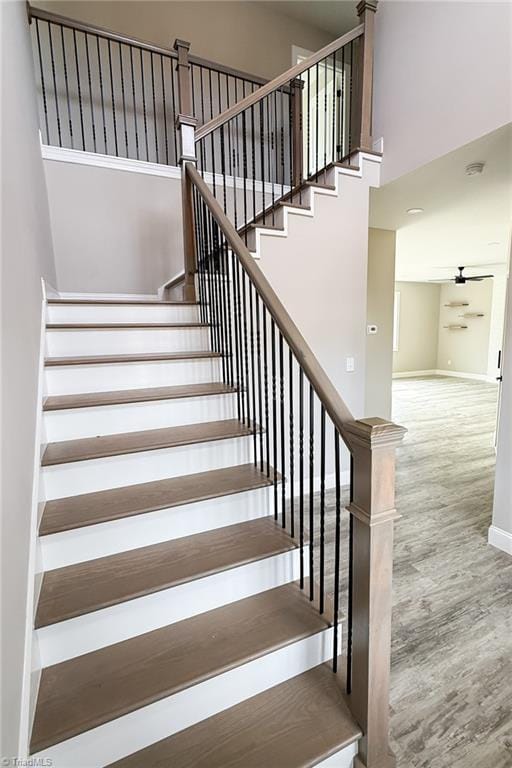 stairway with a high ceiling, baseboards, and wood finished floors