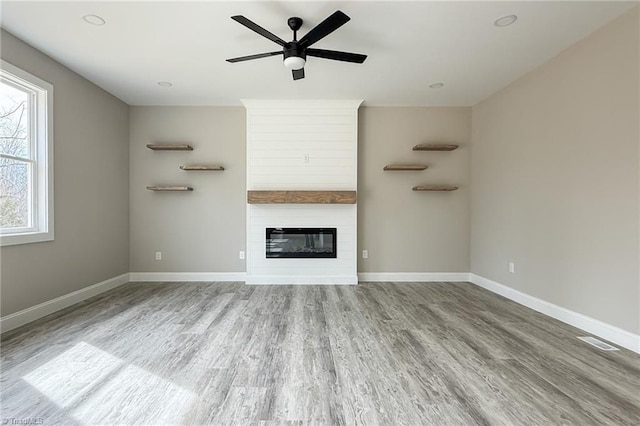 unfurnished living room with visible vents, a large fireplace, baseboards, and wood finished floors