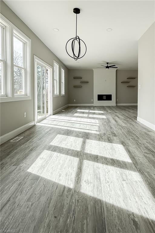 unfurnished living room with a ceiling fan, wood finished floors, visible vents, baseboards, and a fireplace