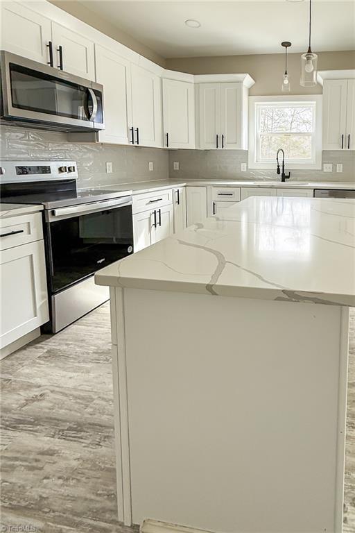 kitchen with backsplash, hanging light fixtures, white cabinets, stainless steel appliances, and a sink