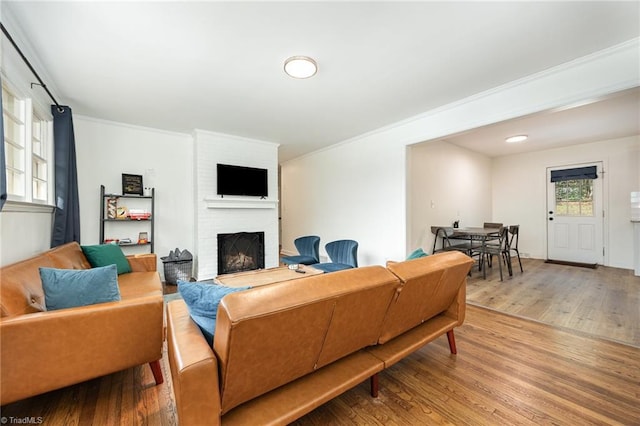 living area with ornamental molding, a brick fireplace, and wood finished floors