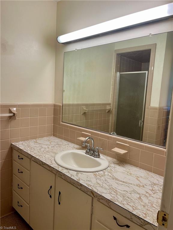 bathroom featuring a shower with shower door, vanity, and tile walls