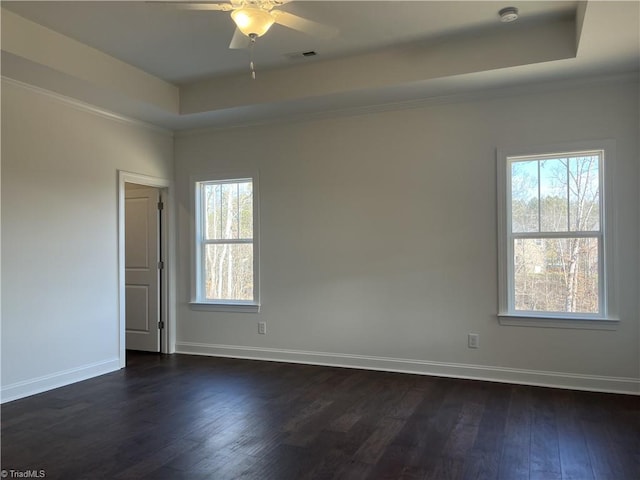 spare room featuring a tray ceiling, baseboards, visible vents, and dark wood finished floors