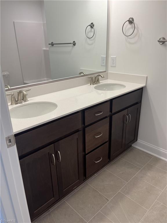 bathroom with a sink, baseboards, double vanity, and tile patterned flooring