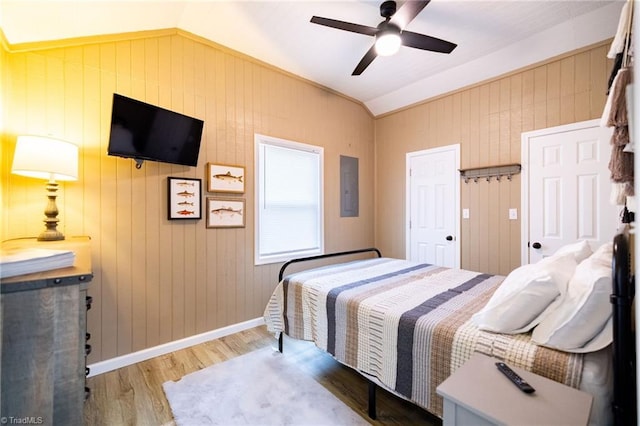 bedroom featuring a ceiling fan, electric panel, wood finished floors, baseboards, and vaulted ceiling