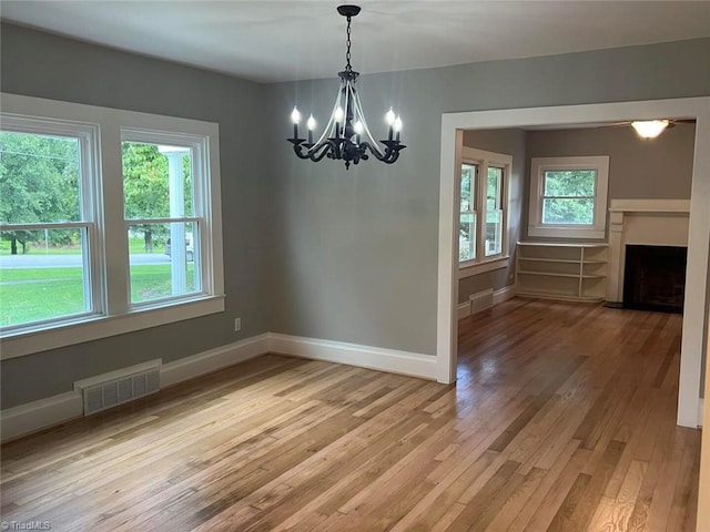 unfurnished dining area featuring visible vents, a fireplace, light wood-type flooring, and baseboards