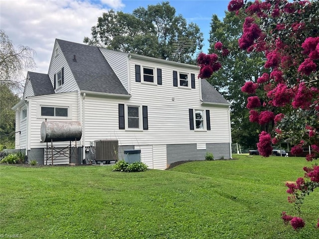 back of house featuring heating fuel, cooling unit, a yard, and a shingled roof