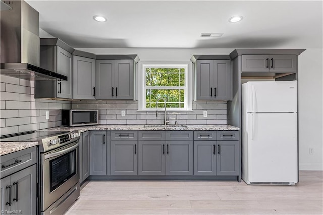 kitchen featuring wall chimney range hood, appliances with stainless steel finishes, gray cabinetry, and sink