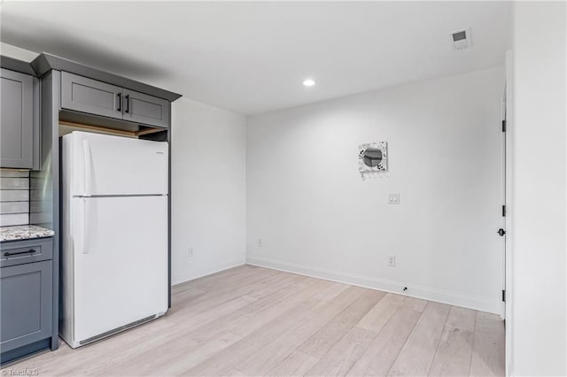 kitchen with gray cabinets, light hardwood / wood-style floors, white refrigerator, and light stone countertops