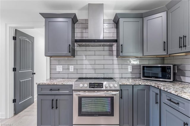 kitchen with light stone countertops, wall chimney range hood, appliances with stainless steel finishes, and tasteful backsplash