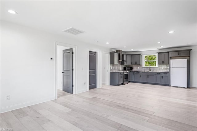 kitchen with wall chimney range hood, stainless steel appliances, light hardwood / wood-style floors, backsplash, and gray cabinetry