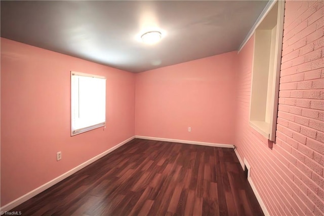 unfurnished room with dark wood-type flooring, baseboards, and brick wall