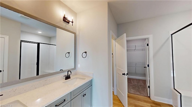 3043 Loch Dr, Winston-Salem, NC 27106 - bathroom featuring wood finished floors, a shower stall, double vanity, a walk in closet, and baseboards