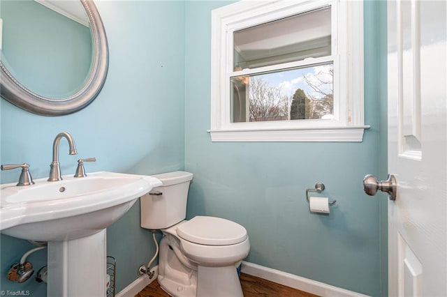 half bathroom featuring toilet, wood finished floors, baseboards, and a sink