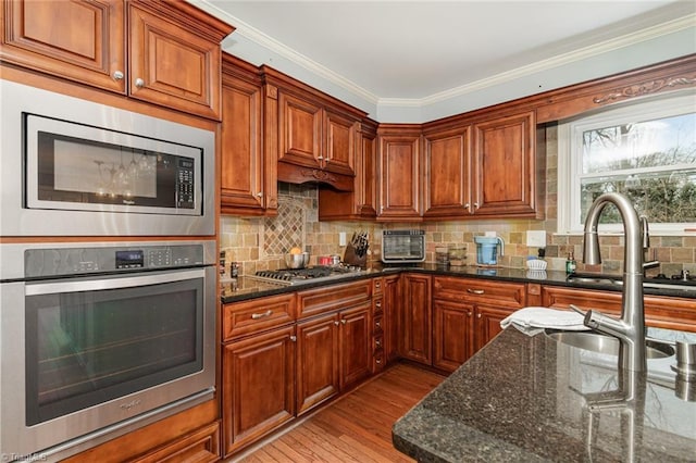 kitchen with decorative backsplash, dark stone countertops, stainless steel appliances, and light wood-style floors