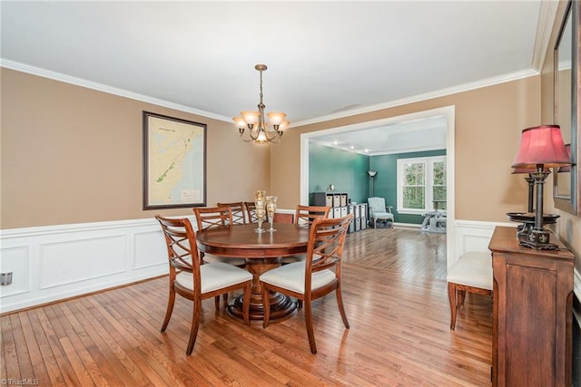 dining room with light wood finished floors, a notable chandelier, crown molding, and a wainscoted wall