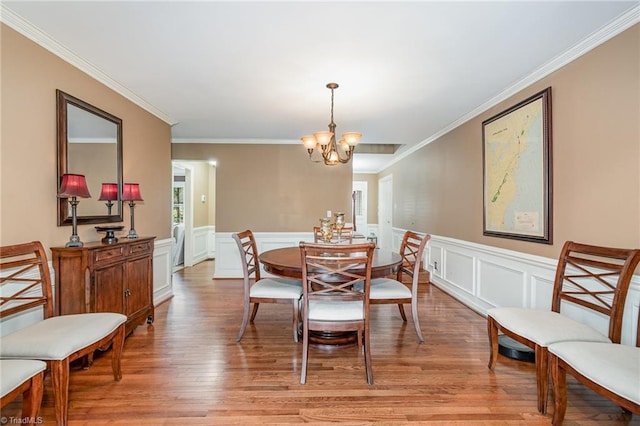 dining room with crown molding, light wood-style flooring, a notable chandelier, and a wainscoted wall