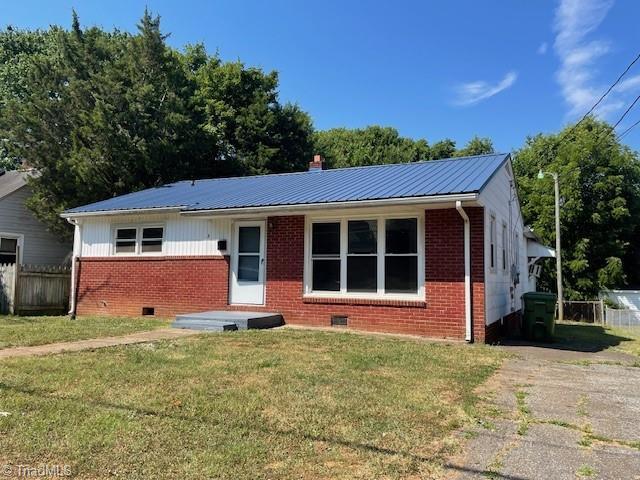 ranch-style home featuring a front lawn, fence, metal roof, crawl space, and brick siding