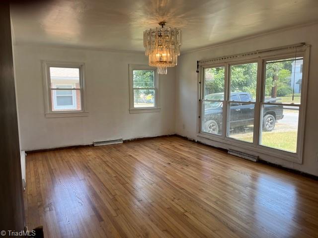 spare room featuring visible vents, a notable chandelier, wood finished floors, and crown molding