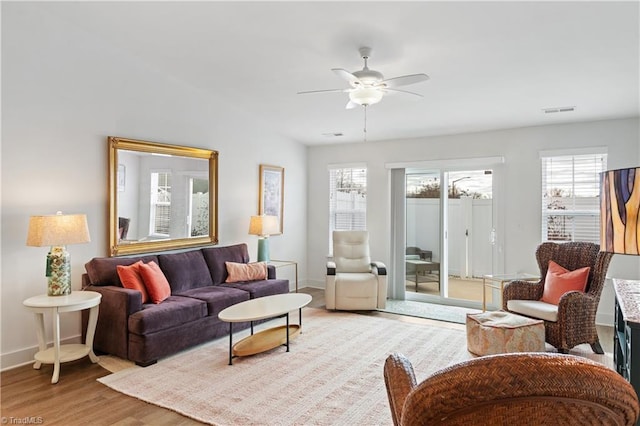 living room featuring a ceiling fan, light wood-style floors, visible vents, and baseboards