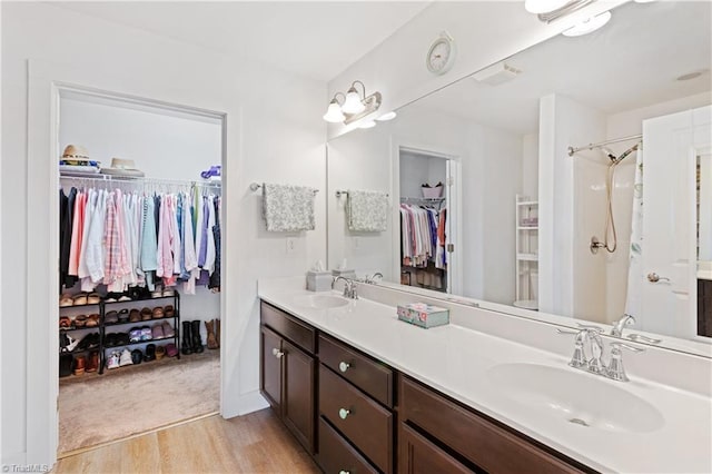 full bathroom with a sink, a walk in closet, wood finished floors, and double vanity