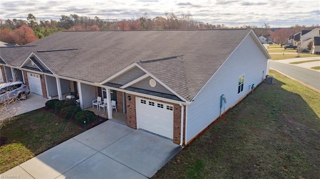 view of front of home featuring a front yard, driveway, central AC, a garage, and brick siding