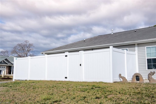 back of house with a yard, a shingled roof, and fence