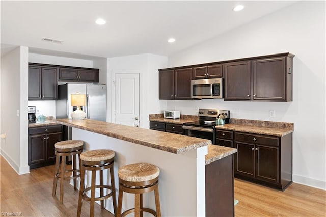 kitchen with a kitchen island, light wood-style floors, appliances with stainless steel finishes, a breakfast bar area, and dark brown cabinets