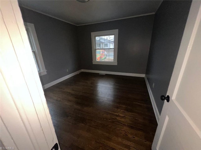 empty room with baseboards, crown molding, and dark wood-type flooring