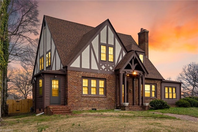 tudor home featuring brick siding, roof with shingles, a chimney, stucco siding, and entry steps