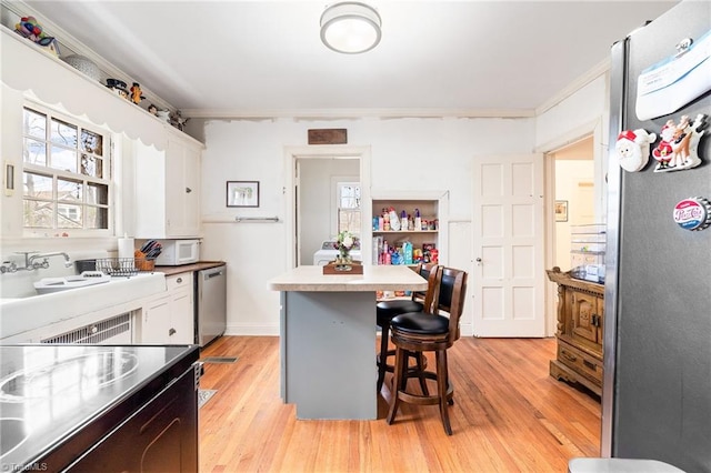 kitchen with appliances with stainless steel finishes, white cabinets, light wood-style floors, and a breakfast bar area