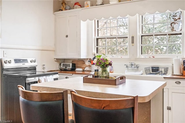 kitchen with white cabinets, light countertops, a breakfast bar area, and stainless steel electric stove