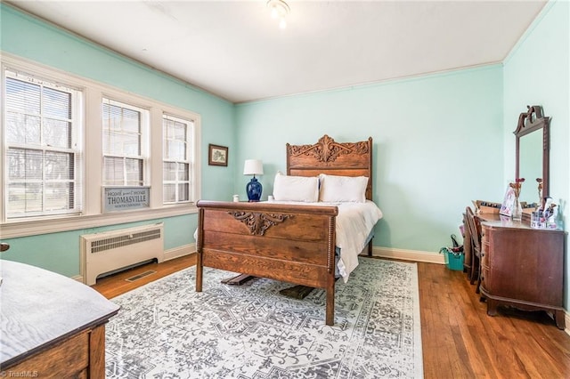 bedroom with baseboards, ornamental molding, wood finished floors, and radiator