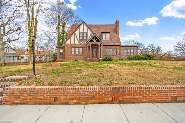 tudor home featuring brick siding, a chimney, stucco siding, and a front yard