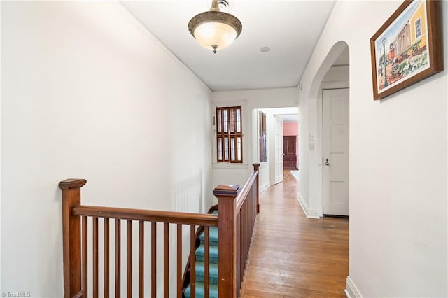 hallway with arched walkways, baseboards, an upstairs landing, and wood finished floors