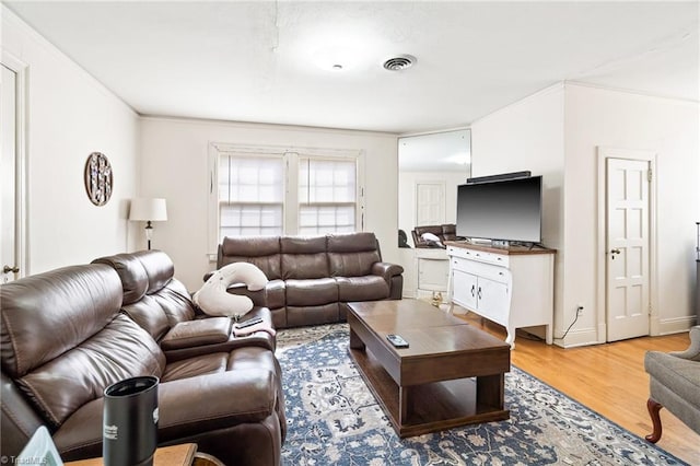 living room with baseboards, light wood finished floors, visible vents, and crown molding