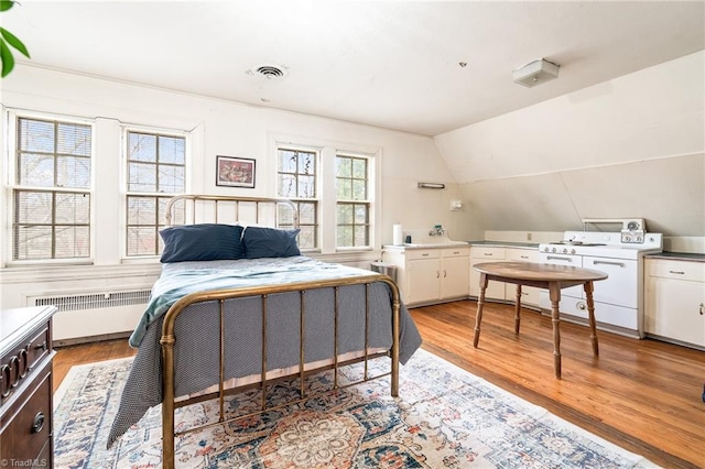 bedroom featuring light wood-type flooring, visible vents, lofted ceiling, and radiator heating unit