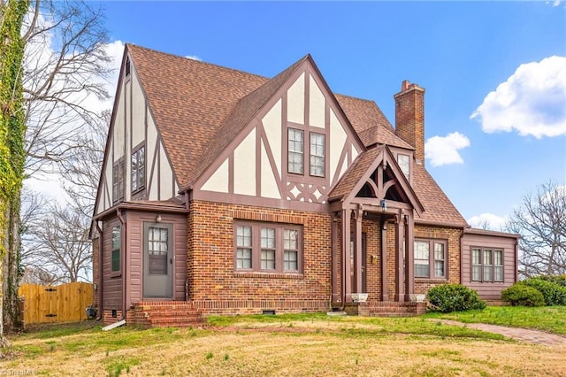 tudor home with entry steps, brick siding, a shingled roof, stucco siding, and a chimney