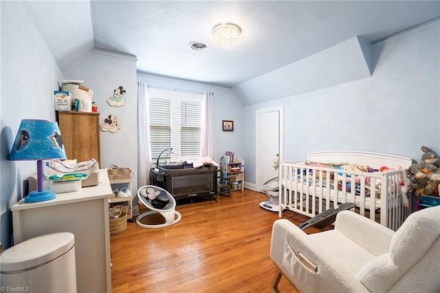 bedroom with wood finished floors, visible vents, baseboards, vaulted ceiling, and a nursery area