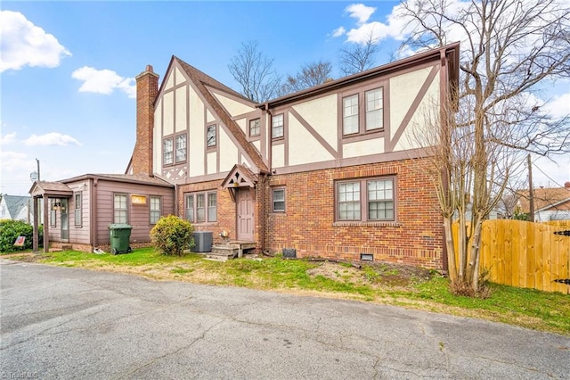 english style home with brick siding, stucco siding, central AC unit, crawl space, and fence