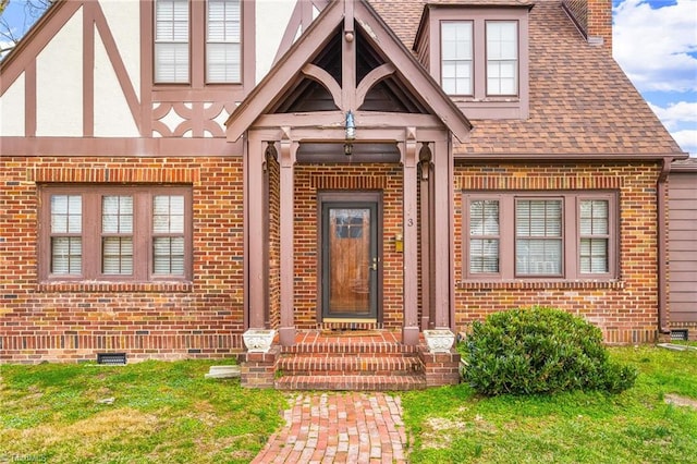 doorway to property with crawl space, brick siding, a lawn, and roof with shingles