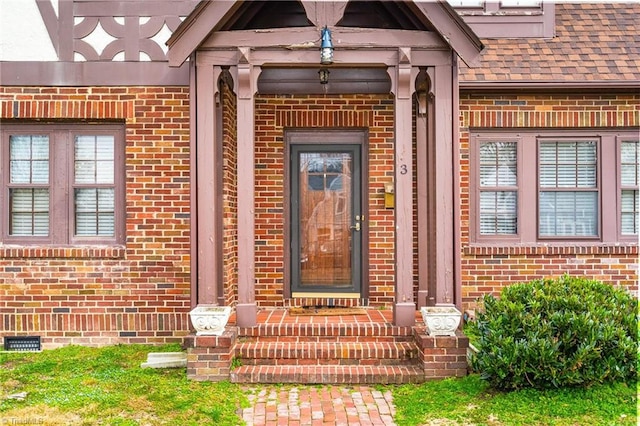 property entrance featuring a shingled roof, crawl space, and brick siding