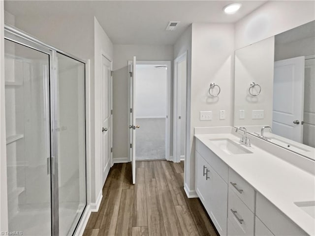 full bathroom with double vanity, a sink, a shower stall, and wood finished floors