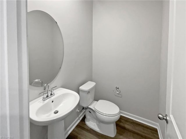 bathroom with toilet, a sink, baseboards, and wood finished floors