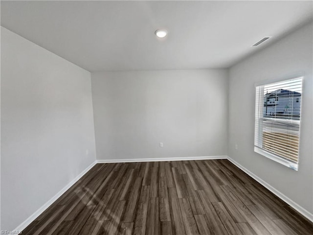 unfurnished room with dark wood-style floors, visible vents, and baseboards