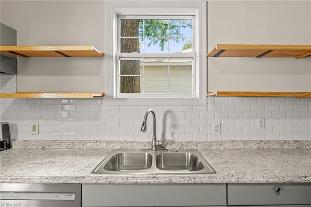 kitchen with stainless steel dishwasher, tasteful backsplash, light stone counters, and sink